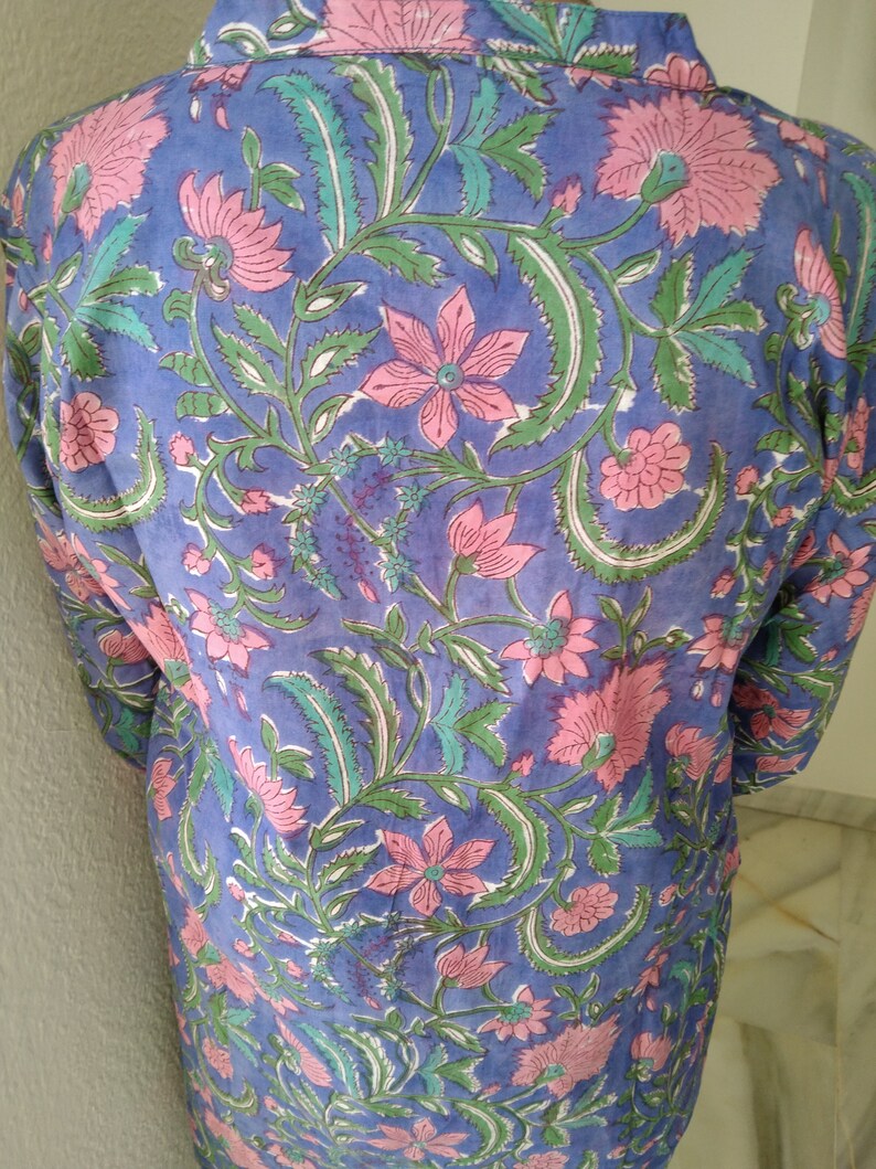 May include: A blue cotton tunic with a floral print in shades of pink and green. The print features a repeating pattern of flowers and leaves.