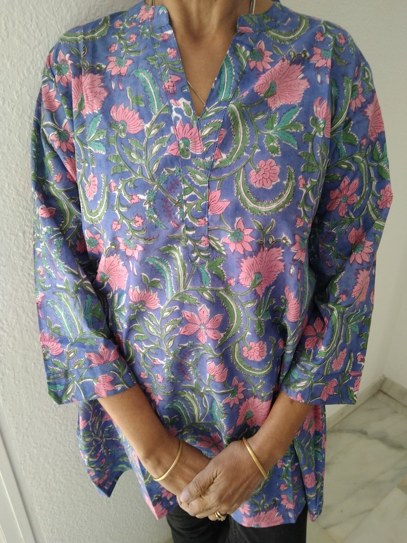 May include: A blue cotton tunic with a floral print in shades of pink and green. The tunic has a V-neck and three-quarter sleeves.