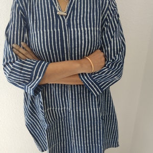 May include: A blue and white striped tunic top with a long sleeve and a v-neck.