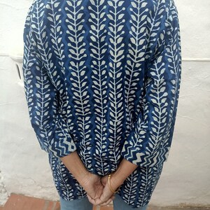 Op de afbeelding: Een langarmige blauwe en witte gepatroneerde tuniek met een staande kraag. De tuniek heeft een bladvormig ontwerp.