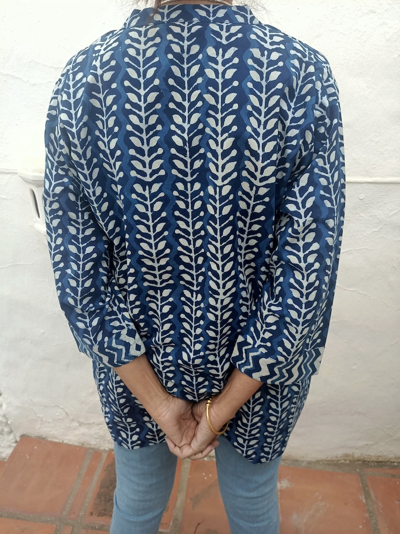 Op de afbeelding: Een langarmige blauwe en witte gepatroneerde tuniek met een staande kraag. De tuniek heeft een bladvormig ontwerp.