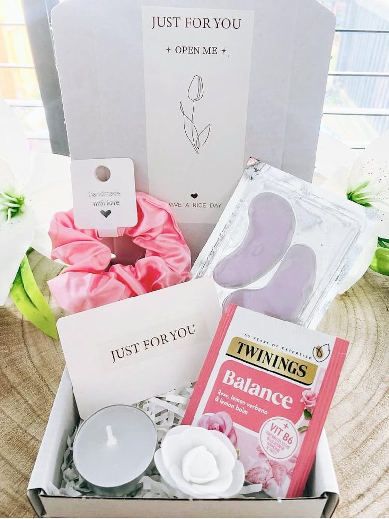 May include: A gift box containing a pink scrunchie, eye patches, a tea bag, a candle, and a decorative flower. The box includes a card that says "JUST FOR YOU" and "+ OPEN ME +" with a tulip illustration. A small tag reads "Handmade with love."