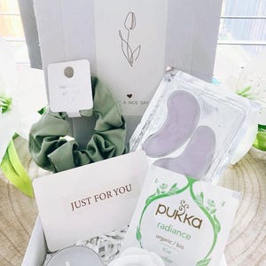 May include: A gift box containing a green scrunchie, eye patches, a tea bag, a white candle, and a decorative flower. The box includes a card that says "JUST FOR YOU" and a card that says "Hairpin with love". The box also has a card that says "JUST FOR YOU" and "+ OPEN ME +".