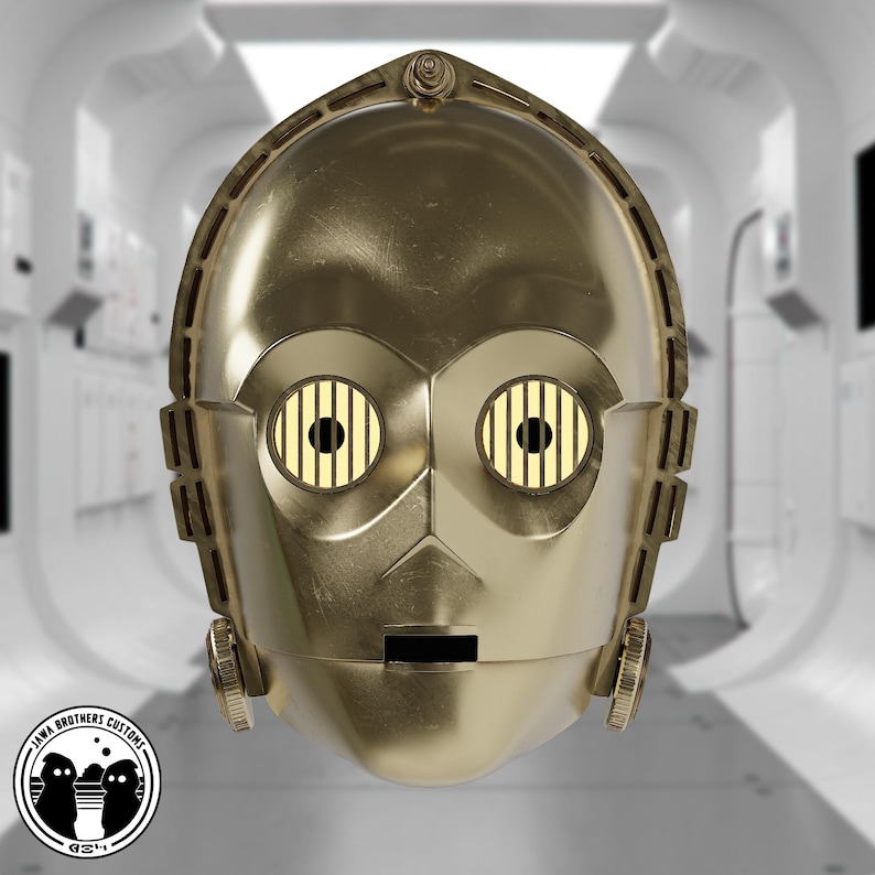 May include: A gold-colored C-3PO head replica with detailed features, including eye sockets with yellow and black grid patterns. The head has a metallic finish and is set against a futuristic, white-walled background. The Jawa Brothers Customs logo is in the lower left corner.