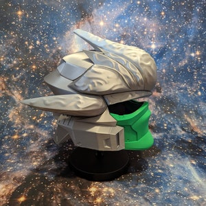 Op de afbeelding: Een 3D-geprinte helm met een zilveren en groene kleurstelling. De helm heeft een futuristisch ontwerp met ingewikkelde details en een vizier.