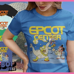 May include: A blue t-shirt with a retro-style graphic of Mickey Mouse and a space creature in front of a planet. The text "EPCOT CENTER" is printed in yellow on the shirt.
