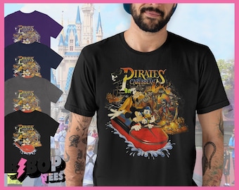 Könnte beinhalten: Schwarzes T-Shirt mit einem Vintage-Grafikdruck von Mickey Mouse und Goofy, die auf einem Boot vor einem Piratenschiff fahren. Der Text "Pirates of the Caribbean" ist über dem Bild gedruckt.