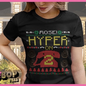 May include: A black t-shirt with a Christmas-themed design featuring a red phone with the number "2" on it. The text "ROSE! HYPER ON" is written in yellow and green on the shirt.