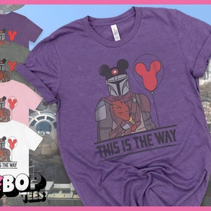 May include: Purple t-shirt featuring a graphic of a Mandalorian wearing Mickey Mouse ears and holding a red balloon. The text "This is the Way" is printed below the graphic.