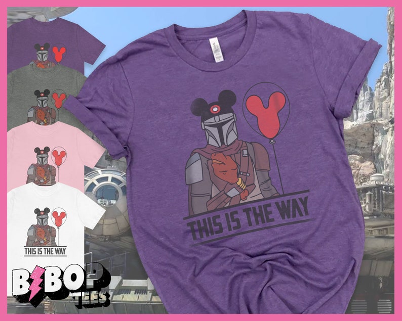 May include: Purple t-shirt featuring a graphic of a Mandalorian wearing Mickey Mouse ears and holding a red balloon. The text "This is the Way" is printed below the graphic.