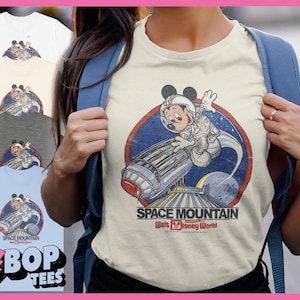 May include: A cream-coloured t-shirt with a distressed graphic of Mickey Mouse in a spacesuit, with the words "Space Mountain" and "Walt Disney World." The design is set within a blue and red circle.