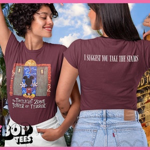 以下が含まれることがあります： 正面に「The Twilight Zone Tower of Terror」の文字とミッキーマウスがドアの前にいるグラフィックがプリントされた、マルーンのTシャツ。Tシャツの背面には「I suggest you take the stairs」の文字がプリントされています。