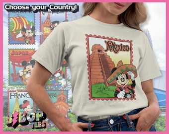 Op de afbeelding: Een wit T-shirt met een vintage-stijl afbeelding van Mickey Mouse die een sombrero draagt en een camera vasthoudt. De afbeelding is geplaatst tegen een achtergrond van een piramide en de tekst "Mexico". Het shirt maakt deel uit van een collectie T-shirts met Mickey Mouse in verschillende landen.