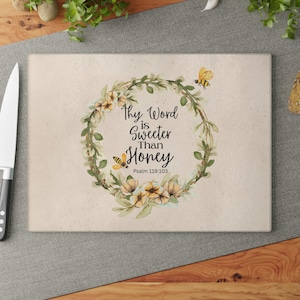 May include: A beige cutting board with a floral wreath design and the text "Thy Word is Sweeter Than Honey" with the scripture reference "Psalm 119:103".