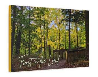 May include: A photograph of a forest path with a wooden bridge and the text "Trust in the Lord" written in white cursive on the ground. The trees are mostly green with some yellow leaves.