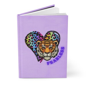 May include: A purple journal with a colorful tiger face inside a heart shape. The words "Fearless" are written in purple below the heart.