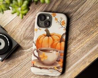 Könnte beinhalten: Eine Handyhülle mit einem herbstlichen Design. Das Case zeigt drei orangefarbene Kürbisse, eine Kaffeetasse und florale Akzente. Der Hintergrund ist cremefarben. Das Case liegt auf einer Holzoberfläche.