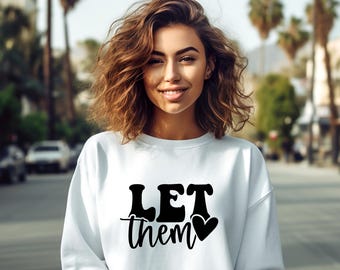 Op de afbeelding: Witte trui met zwarte tekst die "LET them" zegt met een klein zwart hart.
