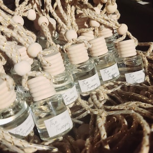 May include: A collection of small, clear glass bottles with wooden caps and white labels. Each bottle is attached to a decorative rope with wooden beads. The labels read "The 2025 Thanpes".