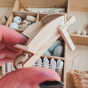Pu&ograve; includere: Una carriola in legno in miniatura, parte di un set artigianale. La carriola &egrave; in legno di colore chiaro e ha una sola ruota. Altri pezzi artigianali in legno, tra cui perline e pezzi di recinzione, sono visibili sullo sfondo. Il set &egrave; in una scatola di legno.