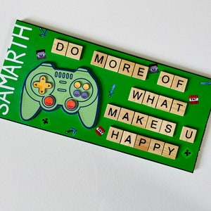 May include: A green wooden sign with the words "Do More Of What Makes You Happy" spelled out in wooden letter tiles. The sign also features a cartoon video game controller, Minecraft-themed graphics, and the name "Samarth" at the top.
