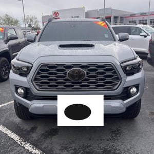 Könnte beinhalten: Ein grauer Toyota Tacoma-Truck mit schwarzem Kühlergrill und schwarzem Toyota-Emblem. Der Truck hat schwarze Scheinwerfer und Nebelscheinwerfer. Die Vorderseite des Trucks ist der Kamera zugewandt.