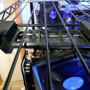 Może przedstawiać: Czarna metalowa obudowa komputera z niebiesko-czarną kartą graficzną. Karta graficzna ma wentylator z niebieskim światłem. Obudowa jest zamontowana na czarnym metalowym stelażu.