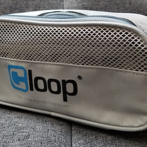 May include: A grey zipped travel bag with a mesh pocket and the word "loop" in black and blue lettering.