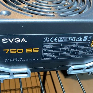 Pode incluir: Uma fonte de alimentação EVGA 750 B5 750W Bronze Switching Power Supply preta com um suporte de metal prateado. A fonte de alimentação tem um rótulo com especificações, incluindo a entrada de CA, a saída de CC e a saída máxima.