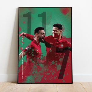 May include: A digital illustration of two soccer players celebrating a goal. The players are wearing red and green jerseys with the numbers 11 and 7. The background is a green and red watercolor effect.