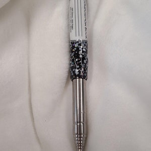 以下が含まれることがあります： 黒と白の斑点模様のキャップが付いた銀色の伸縮式ペン。キャップには、「COMPOSITION BOOK」と「100 Sheets - 200 Pages」と「8 1/2" x 11" 1/2" Wide Ruled」と書かれた白いラベルが付いています。