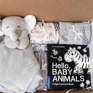 May include: A gift box containing a gray plush elephant security blanket, two folded fabric items with animal prints, and a black and white board book titled Hello, BABY ANIMALS A High-Contrast Book with art by Julissa Mora.