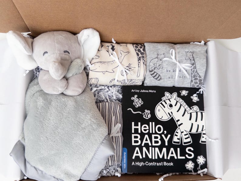 May include: A gift box containing a gray plush elephant security blanket, two folded fabric items with animal prints, and a black and white board book titled Hello, BABY ANIMALS A High-Contrast Book with art by Julissa Mora.