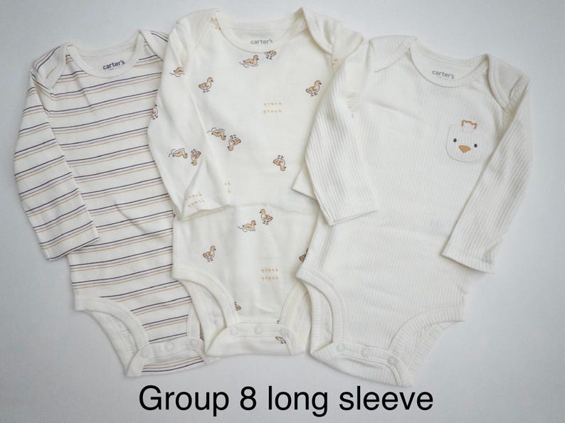 May include: Three long-sleeve Carter's bodysuits. One features horizontal stripes in brown and blue. Another has a repeating pattern of small ducks. The third is solid cream with a small duck graphic on a chest pocket. Text reads: Group 8 long sleeve.