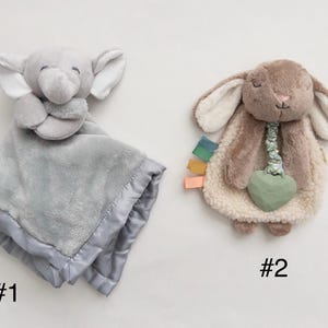 May include: Two plush security blankets. Number 1 is a gray elephant with a soft fabric body and satin trim. Number 2 is a brown rabbit with a textured cream-colored body, a green heart-shaped teether, and small colorful fabric tags on the side.