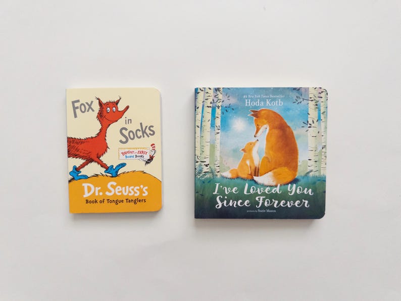 Puede incluir: Dos libros de cart&oacute;n con portadas ilustradas. El libro de la izquierda se titula Fox in Socks de Dr. Seuss, mostrando un zorro rojo con calcetines azules. El libro de la derecha se titula I've Loved You Since Forever de Hoda Kotb, representando a dos zorros en un bosque.