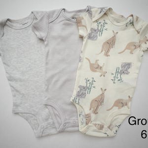 May include: Three short-sleeve baby bodysuits. One is solid light gray, one is light gray with thin horizontal stripes, and one is cream with a pattern of brown kangaroos, gray koalas, and green bamboo stalks. The text Group 6 is visible.