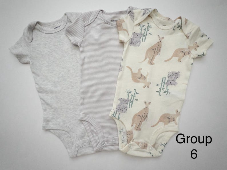 May include: Three short-sleeve baby bodysuits. One is solid light gray, one is light gray with thin horizontal stripes, and one is cream with a pattern of brown kangaroos, gray koalas, and green bamboo stalks. The text Group 6 is visible.