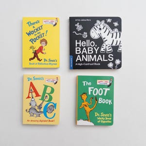 May include: Four board books arranged in a grid. Top left: yellow cover, There's a Wocket in my Pocket! Top right: black cover, Hello, Baby Animals. Bottom left: yellow cover, Dr. Seuss's ABC. Bottom right: green cover, The Foot Book.