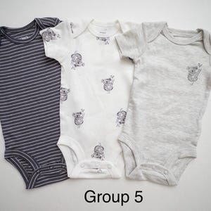May include: Three short-sleeve baby bodysuits labeled Group 5. One is dark gray with white horizontal stripes, one is white with a repeating koala print, and one is solid light gray with a single small koala graphic on the chest.