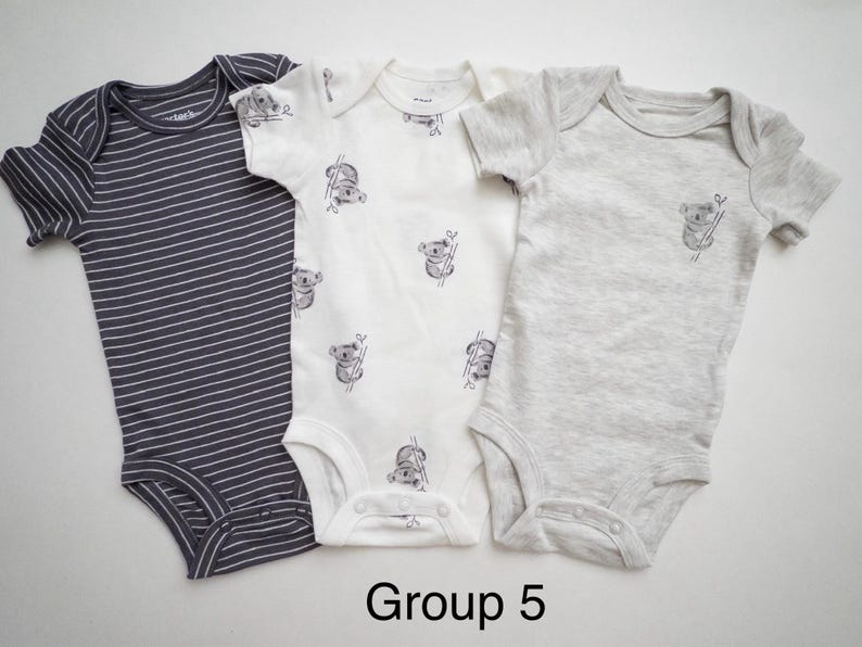 May include: Three short-sleeve baby bodysuits labeled Group 5. One is dark gray with white horizontal stripes, one is white with a repeating koala print, and one is solid light gray with a single small koala graphic on the chest.