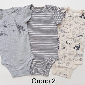 May include: Three short-sleeved baby bodysuits. The left is heather gray with animal illustrations and the text "be kind to all kinds". The center is gray and white striped. The right is cream with a dark animal print pattern. Text "Group 2" below.