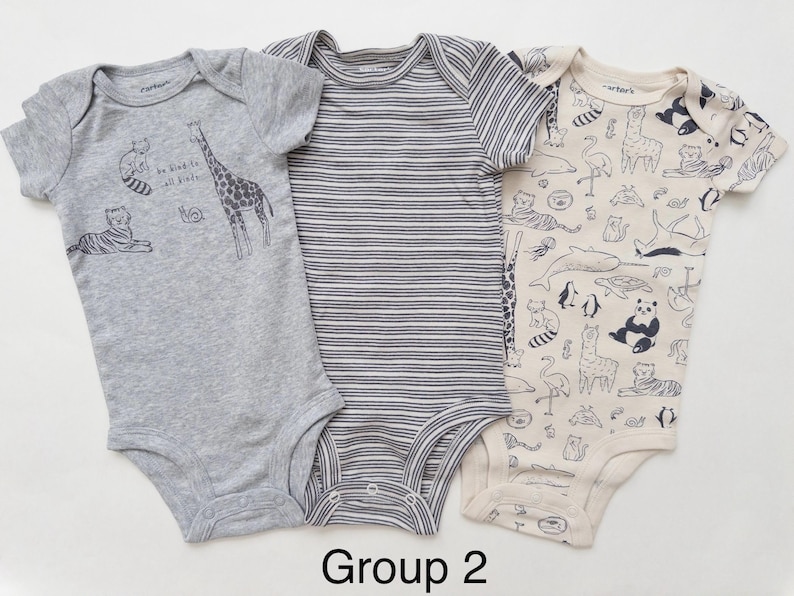 May include: Three short-sleeved baby bodysuits. The left is heather gray with animal illustrations and the text "be kind to all kinds". The center is gray and white striped. The right is cream with a dark animal print pattern. Text "Group 2" below.