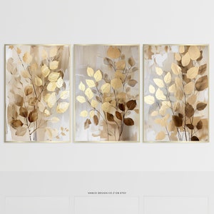 Könnte beinhalten: Ein Set aus drei abstrakten Kunstdrucken mit goldenen und braunen Blättern auf beigefarbenem Hintergrund. Die Drucke sind in Gold gerahmt.