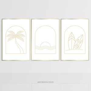 May include: A triptych of framed art prints with minimalist line drawings. The prints show a palm tree, a sunset over the sea, and two surfboards. The artwork is gold on white, with gold frames. The text "VANCO DESIGN CO // ON ETSY" is at the bottom of the prints.