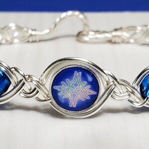 Puede incluir: Una pulsera de alambre plateado con un dije de estrella de vidrio azul y dos acentos de cristal azul.