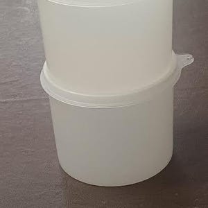 Könnte beinhalten: Zwei weiße Kunststoff-Lebensmittelbehälter, die übereinander gestapelt sind. Jeder Behälter hat einen Deckel und kleine Griffe. Die Behälter sind zylindrisch geformt.