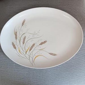 Könnte beinhalten: Ovale, cremefarbene Servierplatte mit einem Weizenähren-Design. Die Ähren sind in Braun-, Gold- und Grautönen gehalten, mit zarten Linien und Details. Ein klassisches Stück zum Servieren von Speisen.