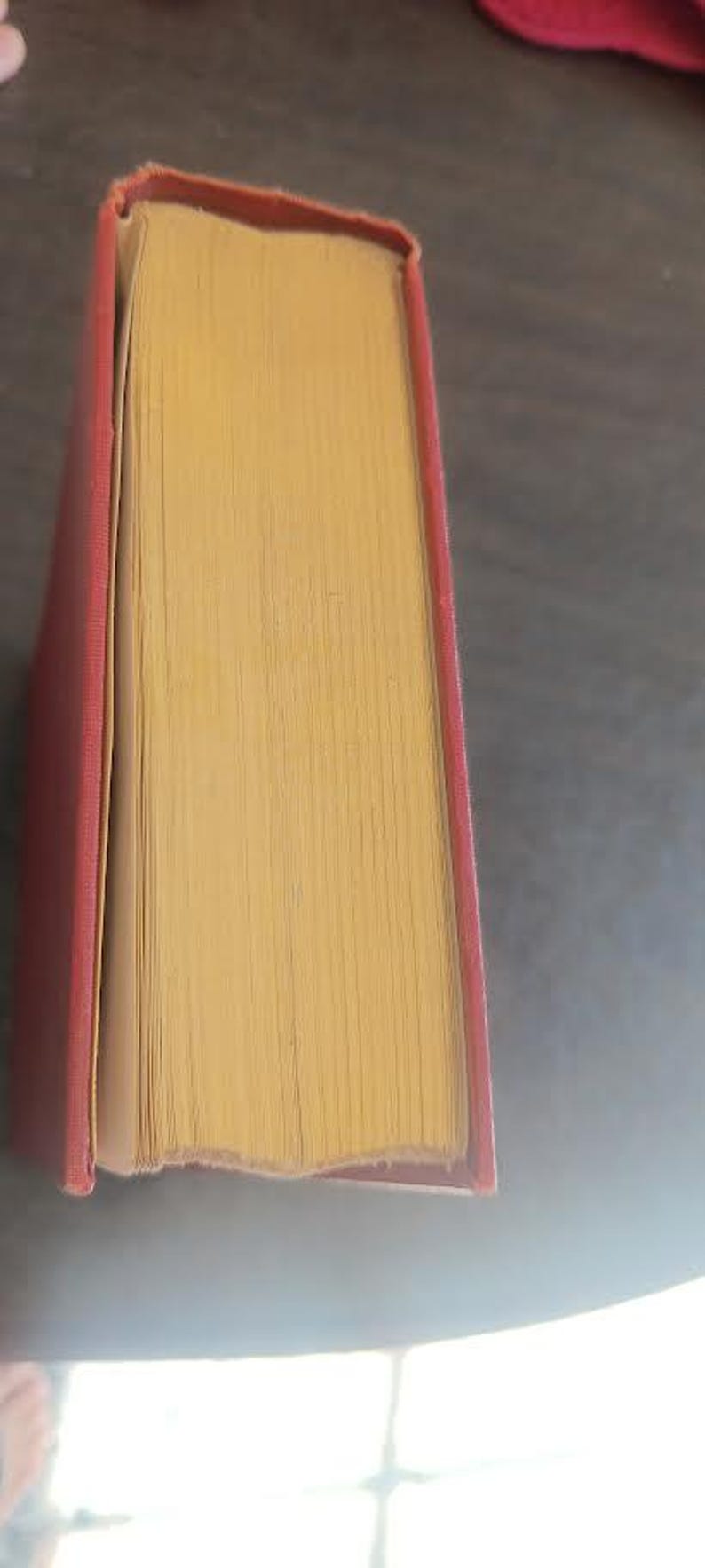 May include: A vintage hardcover book with a red cover and yellowed pages. The book's pages are visible, showing the texture and age of the paper. The book is likely antique.