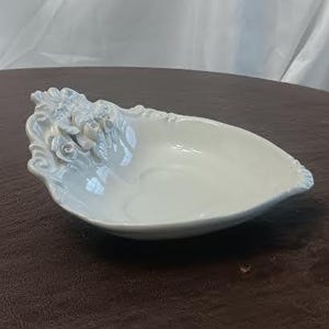 May include: White ceramic decorative dish with a floral design on one end. The dish has a glossy finish and a leaf-like shape. The floral design features detailed roses and leaves.